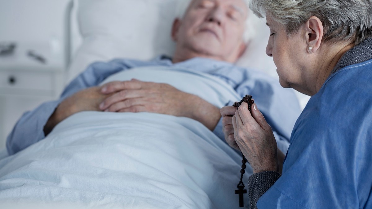 woman praying over man in sickbed
