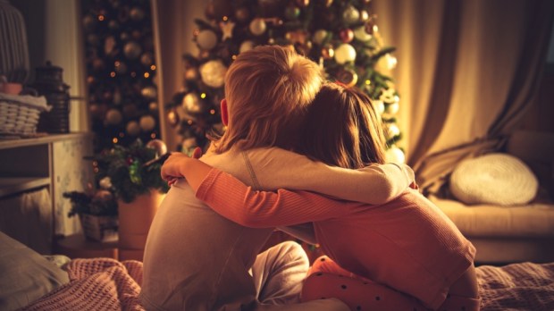 Children sit hugging in bed and look at the Christmas tree
