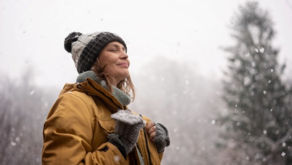 Young mature adult caucasian woman in a hat and yellow jacket breathing fresh air in the winter forest