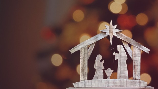 A wooden Christmas Nativity set with the holy family gazing at baby Jesus with a bokeh background