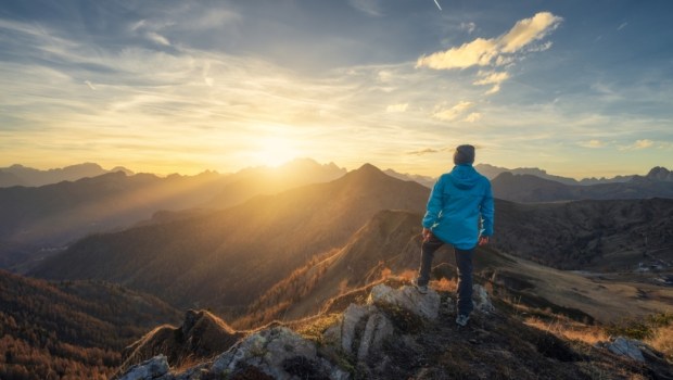 Man on stone on the hill and beautiful mountains in haze at colorful sunset in autumn