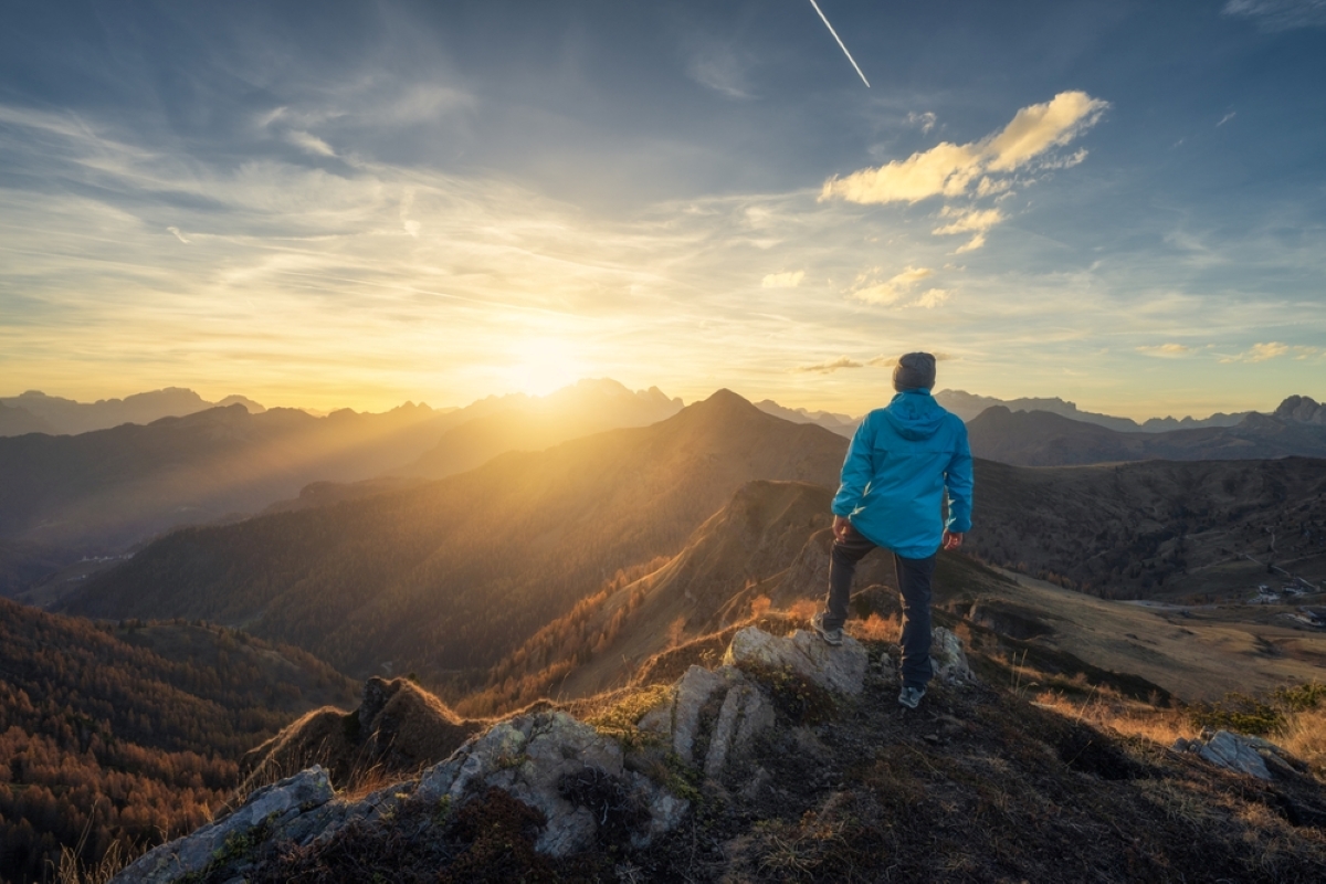 Man on stone on the hill and beautiful mountains in haze at colorful sunset in autumn