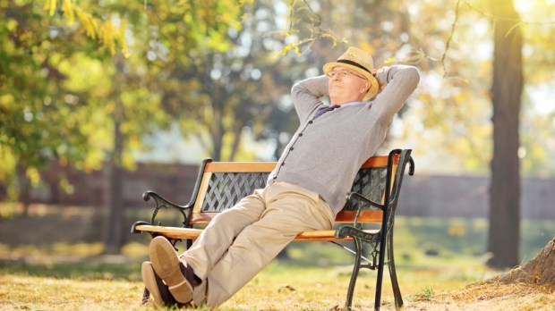 Senior man relaxing in park on a sunny day seated on a wooden bench