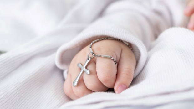close-up detail of a baby's hand at his baptism, holding a christian cross