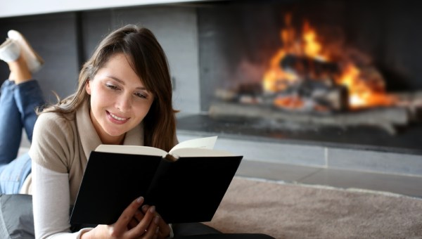 Portrait of beautiful woman reading book by fireplace