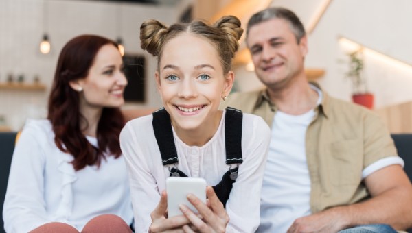 mature parents and teen girl with smartphone in cafe
