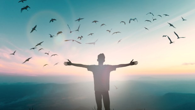 Mężczyzna stoi na szczycie wzgórza z szeroko rozpostartymi rękoma