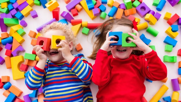 Happy preschool age children play with colorful plastic toy blocks