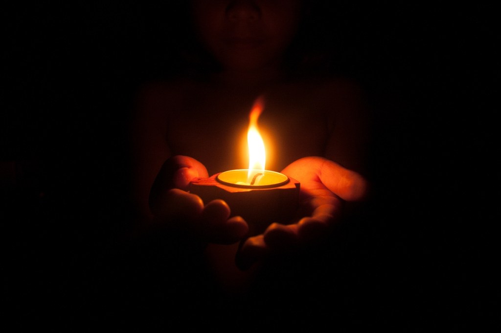 Little child holding burning candle in darkness with noise and grain effect
