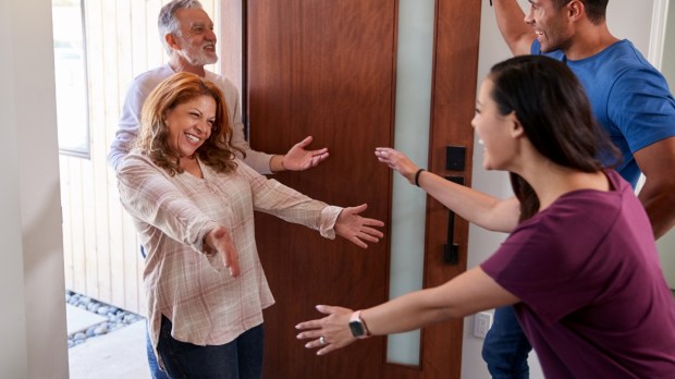 Couple Greeting Senior Parents At Front Door As They Come To Visit