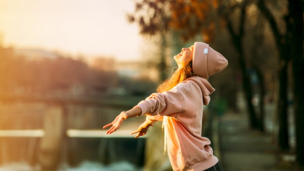 cool hipster young girl in pink hoodie standing by a river