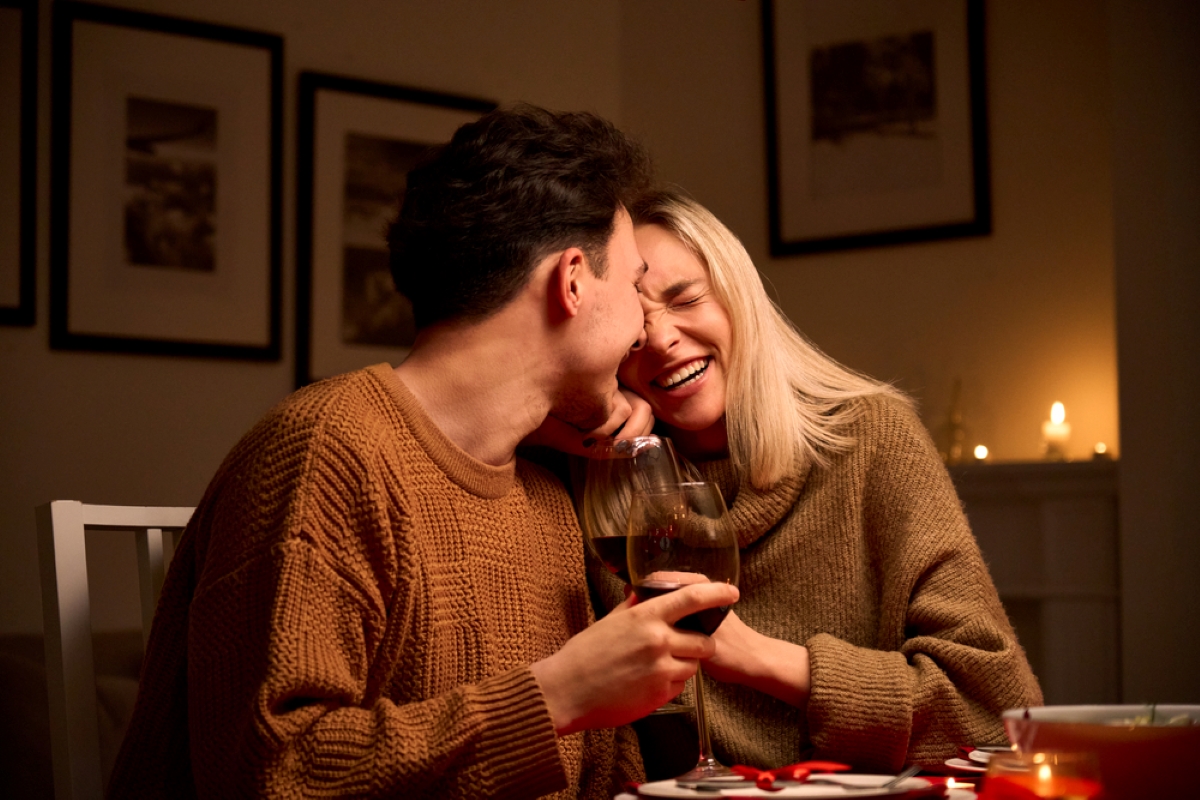 Happy young couple in love hugging, laughing, drinking wine, enjoying talking