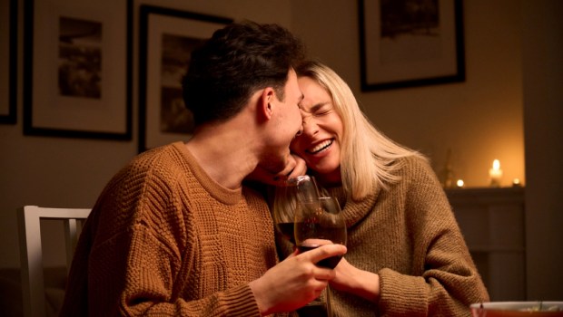 Happy young couple in love hugging, laughing, drinking wine, enjoying talking