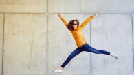 Joyful young lady jumping and raising arms in front of wall outside