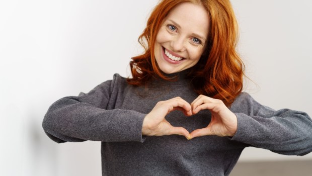 Pretty romantic young redhead woman making a heart gesture