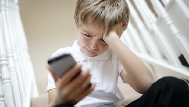 Smutny chłopczyk wpatruje się w telefon