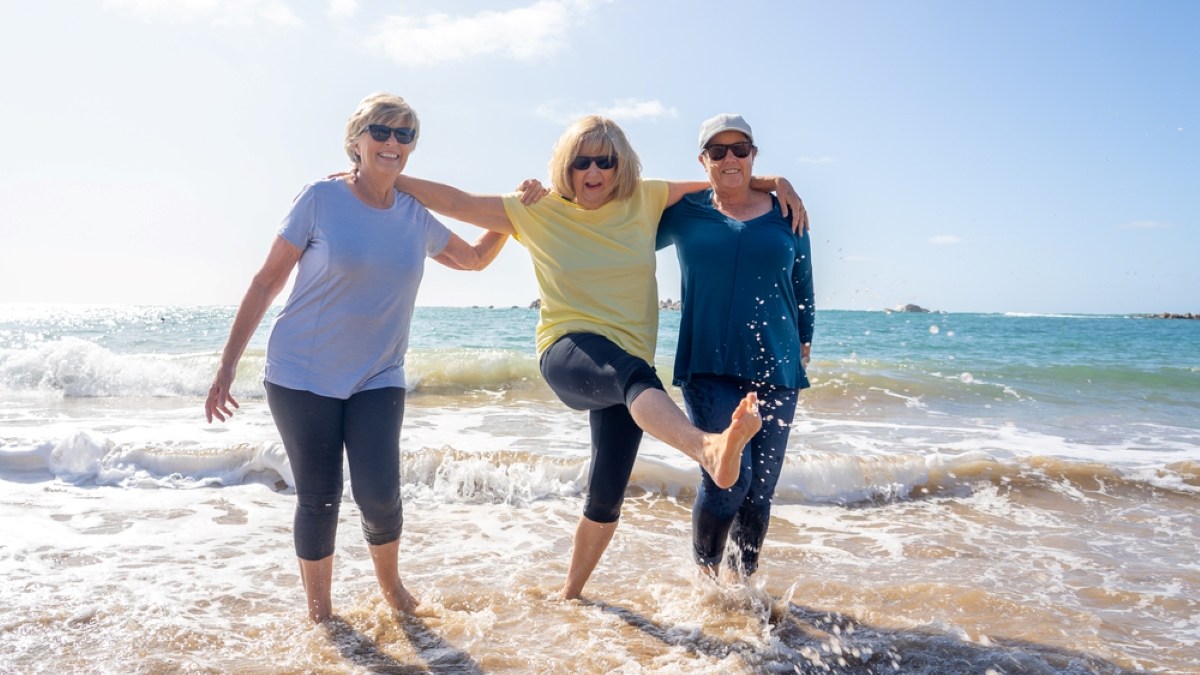 Lovely group of senior girl friends on their 60s walking and having fun splashing water on sea
