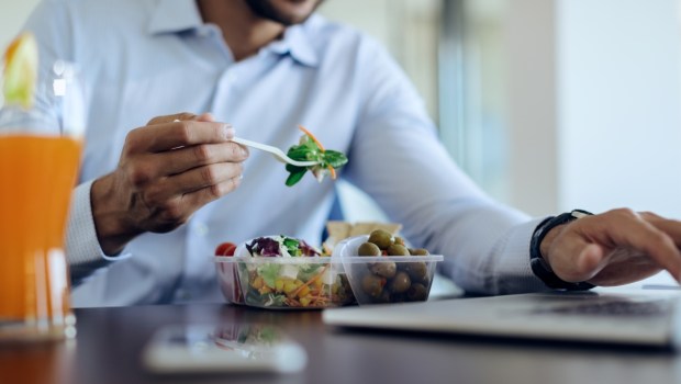 Close-up of businessman eating healthy food while using computer on lunch break in the office