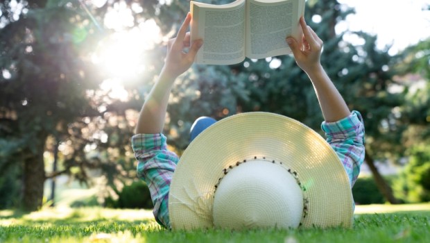 A young woman in a straw hat enjoys spending time reading a book in the park
