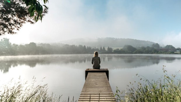 Calm misty morning meditation by pond.Sitting woman outdoors