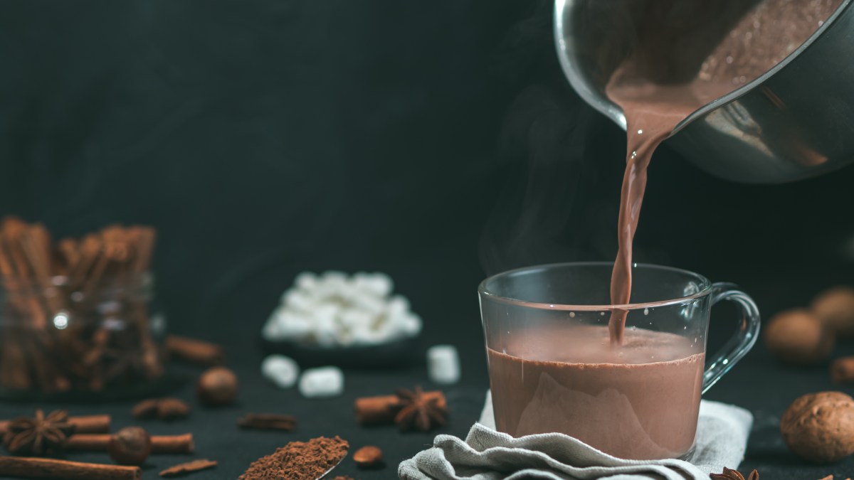 Pouring-tasty-hot-chocolate-cocoa-drink-into-glass-mug-with-ingredients-on-black-table.-Copy-space-Dark-background.-Low-key.-.jpg