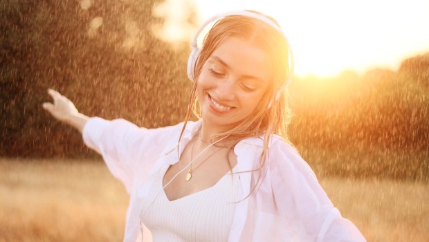 Young beautiful woman dancing in the field and listening music in headphones