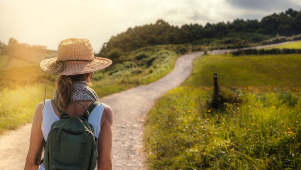 a woman hiker with a straw hat and backpack starts a hike through a meadow in the Basque country