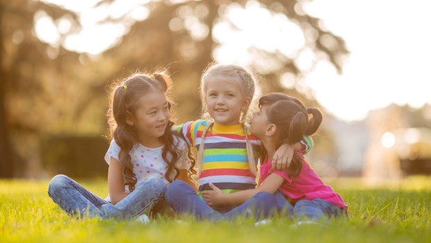 three little girls cuddle in the summer on the lawn