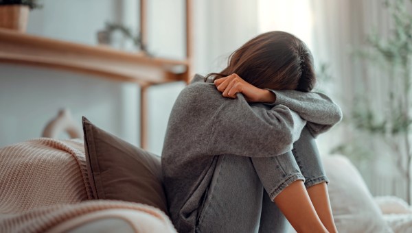 Depressed young woman sitting on couch in the living room at home