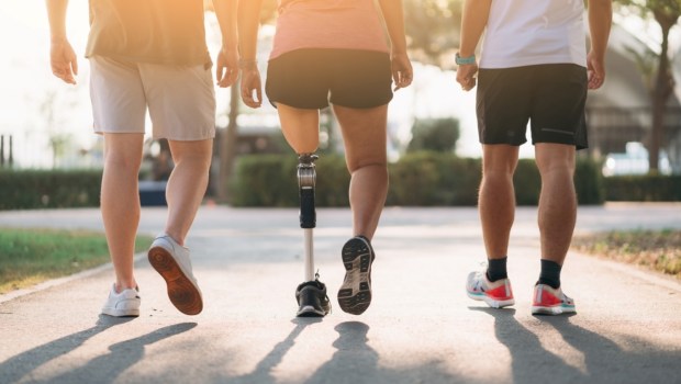 Woman exercising in a park with a friend providing support while using a prosthetic leg