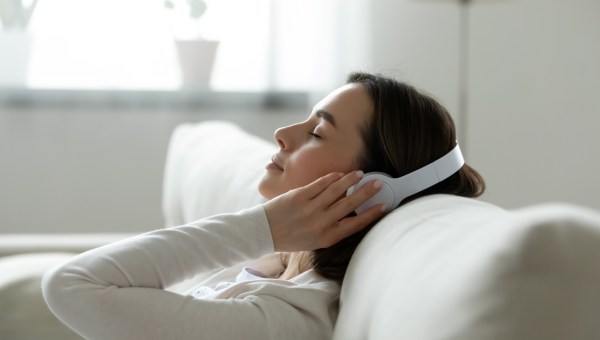 Calm female resting leaned on comfy couch in living room spend free time at home closed eyes enjoy music listening