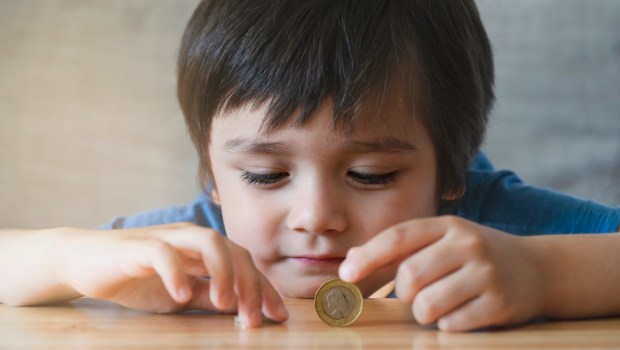 Kid laying head down on wooden try to balancing money coin