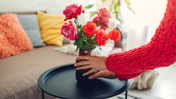 Woman puts vase with flowers roses on table. Housewife taking care of coziness in apartment. Interior design and decor