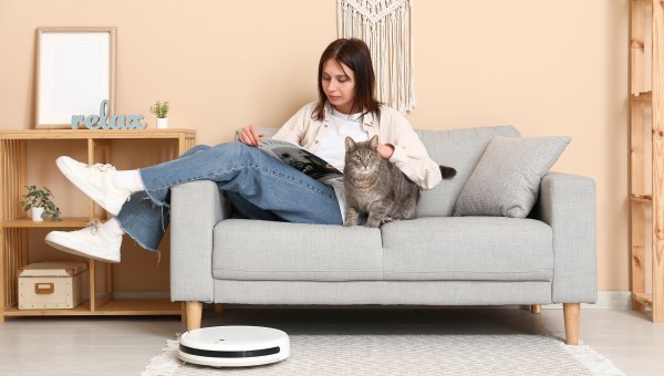 Young woman resting on sofa with cat and robot vacuum cleaner