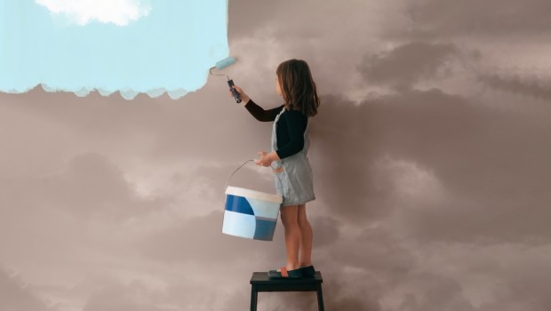 little girl uses a can of paint to color the wall of the room from cloudy gray to clear blue sky