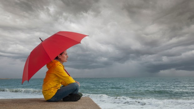 Woman with red umbrella watching storm clouds over the ocean