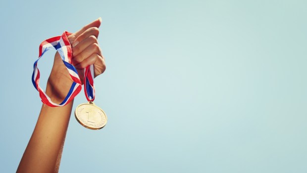 woman hand raised, holding gold medal against sky
