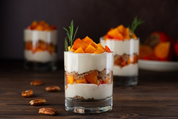 Vegan layered dessert in a glasses with persimmon, rosemary, pecan, whipped cream on a wooden table. Healthy food, sugar, gluten and lactose free.