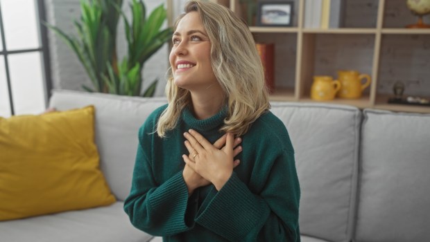 A joyful young caucasian woman places her hands on her heart in a cozy home interior with modern decor