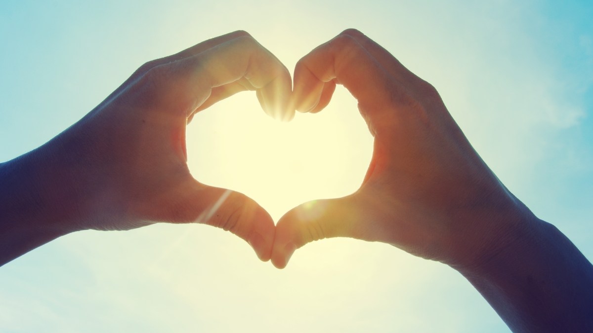 Female hands in the form of heart against the sky pass sun beams