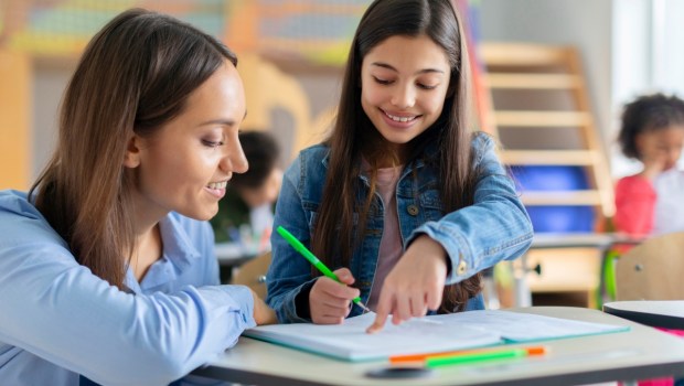 Teacher helping girl in classroom for knowledge, helping schoolgirl and teach her to draw
