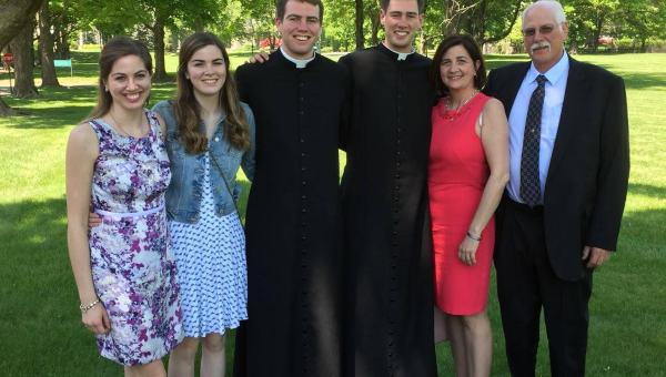 Family posing outside. Two sons in the middle in cassocks.