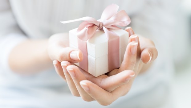 Close up shot of female hands holding a small gift wrapped with pink ribbon
