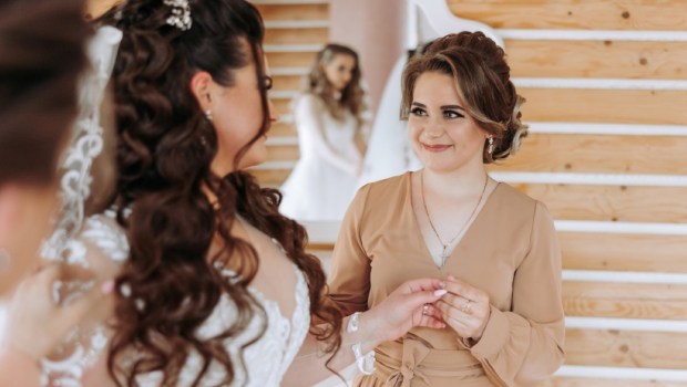 The bride's maid of honor helps the bride lace up her dress