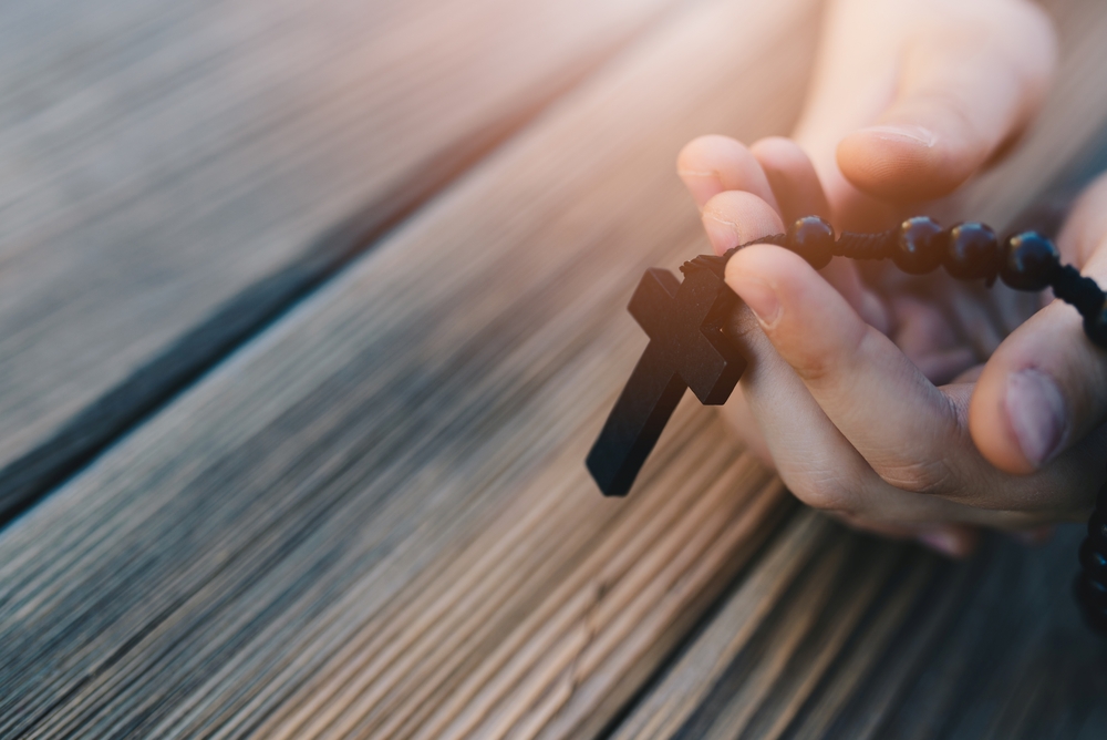 Little childs hands holding wooden rosary. Child praying