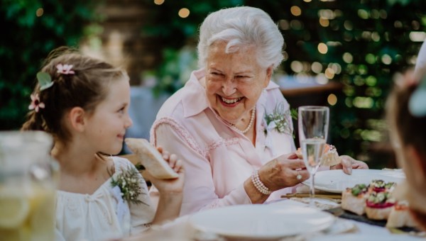 Wedding guests sitting by table, eating and drinking at reception outside in the backyard.