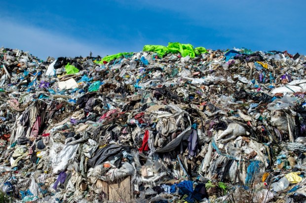 A vast accumulation of discarded clothing and fabrics fills the landfill