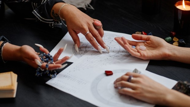 Close up of fortune teller pointing at astrology chart during spiritual seance with young woman