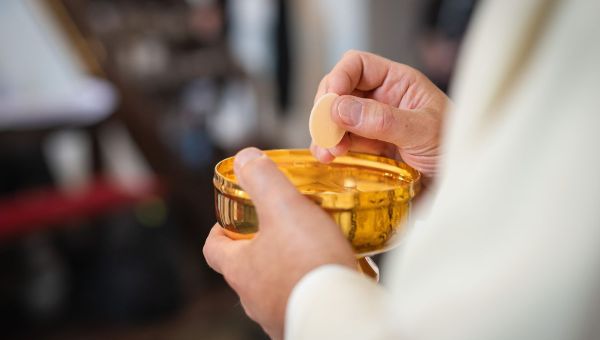A priest holding a golden chalice and a wafer in his hands while distributing Holy Communion in Poland
